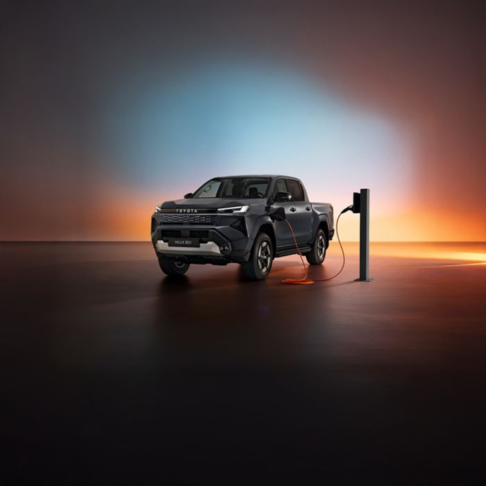 Seitenansicht des neuen vollelektrischen Toyota Hilux, der an einer Ladesäule lädt, mit buntem Hintergrund.