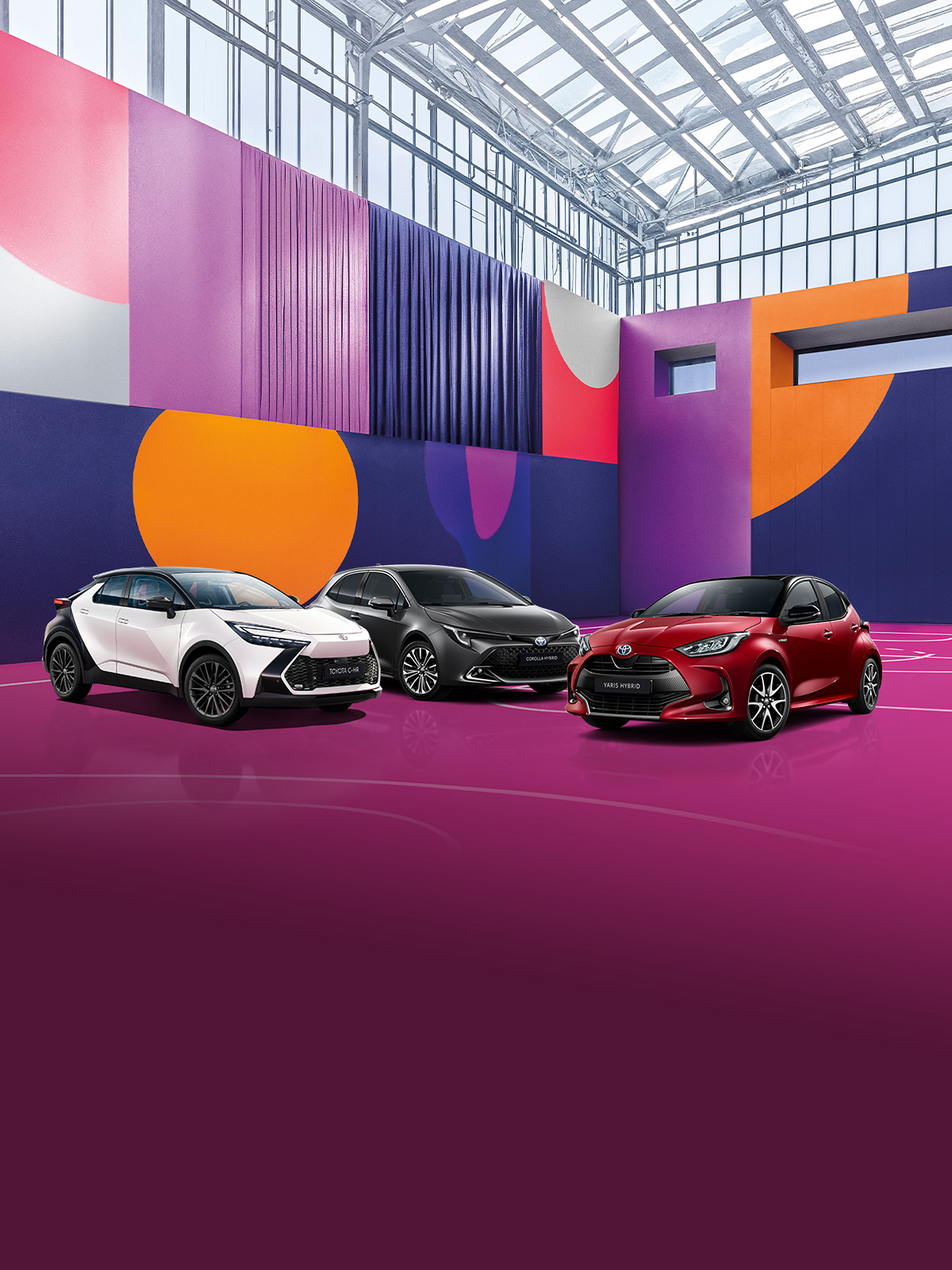 Ein weißer Toyota C-HR, ein grauer Corolla und ein roter Aygo X stehen auf einem pinken Basketballplatz