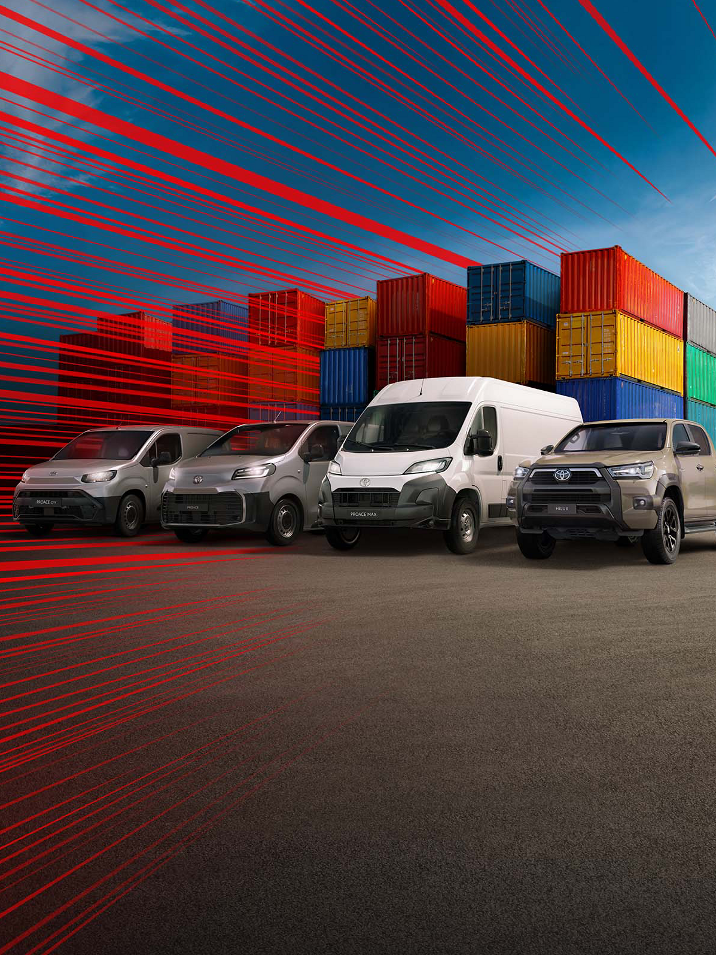 Hilux, Proace Max, Proace und ein Proace City schräg von vorn auf einem Parkplatz, umgeben von Stapeln aus Europaletten, daneben Ladesäulen