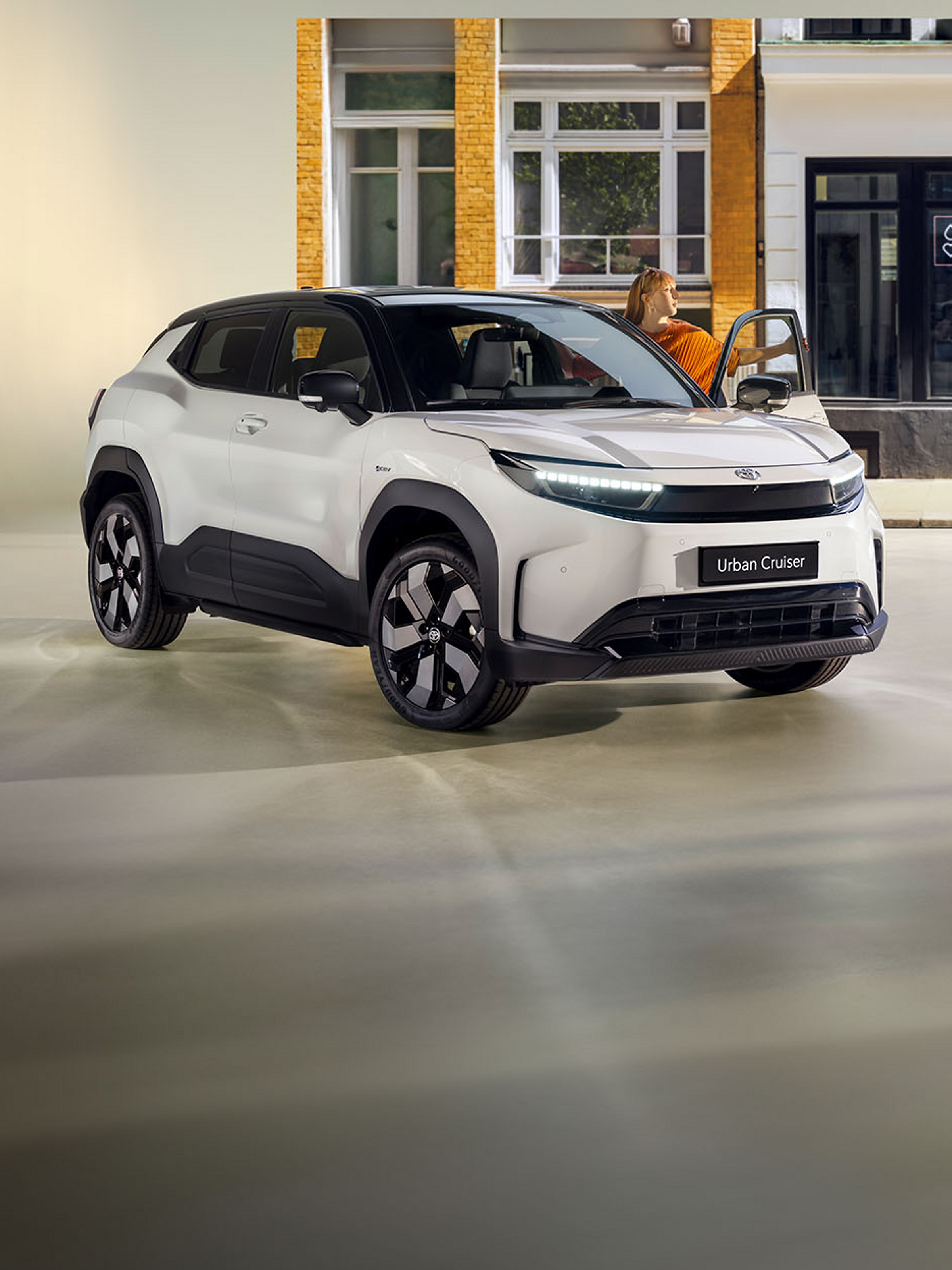 Ein weißer Toyota Urban Cruiser steht vor einer Ladenstraße, während eine Frau aus der Beifahrertür aussteigt.