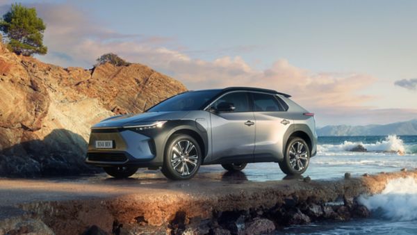 Ein silbergrauer Toyota bZ4X steht an einer Felsenküste, an der sich die Ozeanwellen brechen.