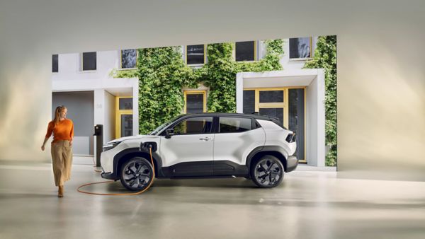 Weißer Mini-SUV steht in einem Studio vor einem Ausschnitt einer Häuserwand an einer Ladesäule.