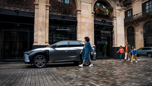 Person läuft zur Fahrertür eines am Straßenrand geparkten SUV-Auto mit Elektroantrieb, das gerade an einer Ladesäule lädt.