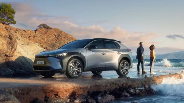 Zwei Personen stehen auf einem Felsen an der Meeresküste und genießen die frische Luft. Dahinter steht ein elektrischer silberner SUV.