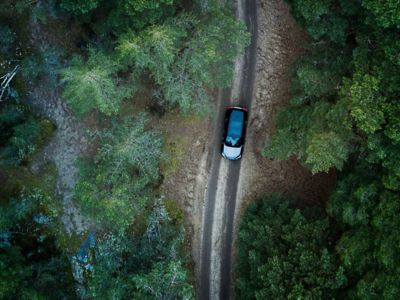 Drohnenaufnahme eines SUV-Autos, das auf einer Schotterstraße durch einen dichten Wald fährt