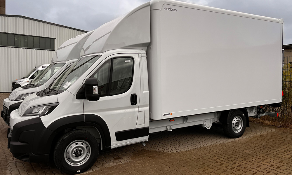 Weißer Toyota Transporter mit Kofferaufbau vor einem Werkstattgebäude.