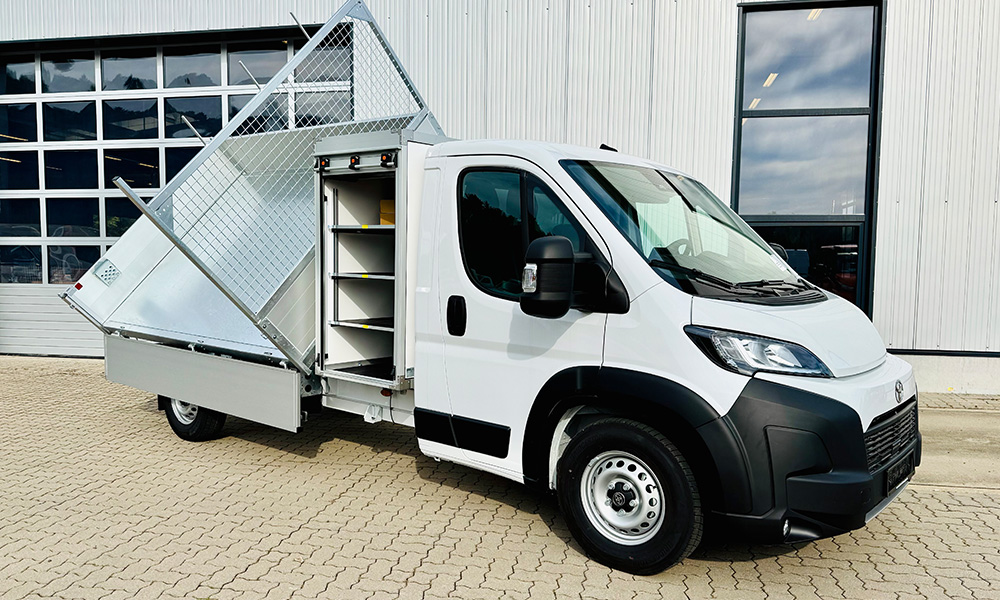 Weißer Toyota Transporter mit Kipper-Aufbau vor einem Werkstattgebäude.
