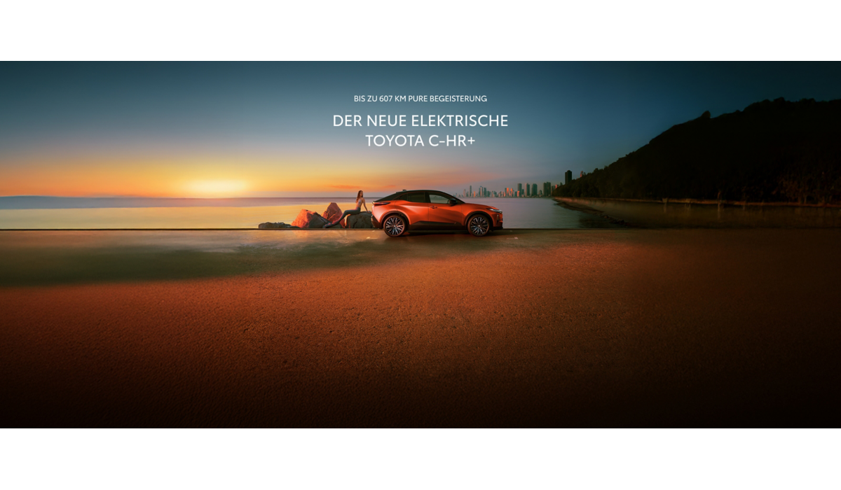 Ein orangefarbener C-HR+ steht bei Sonnenuntergang an einer Küstenstraße; eine Person sitzt entspannt auf Felsen daneben, im Hintergrund sind Meer und eine Skyline zu sehen.