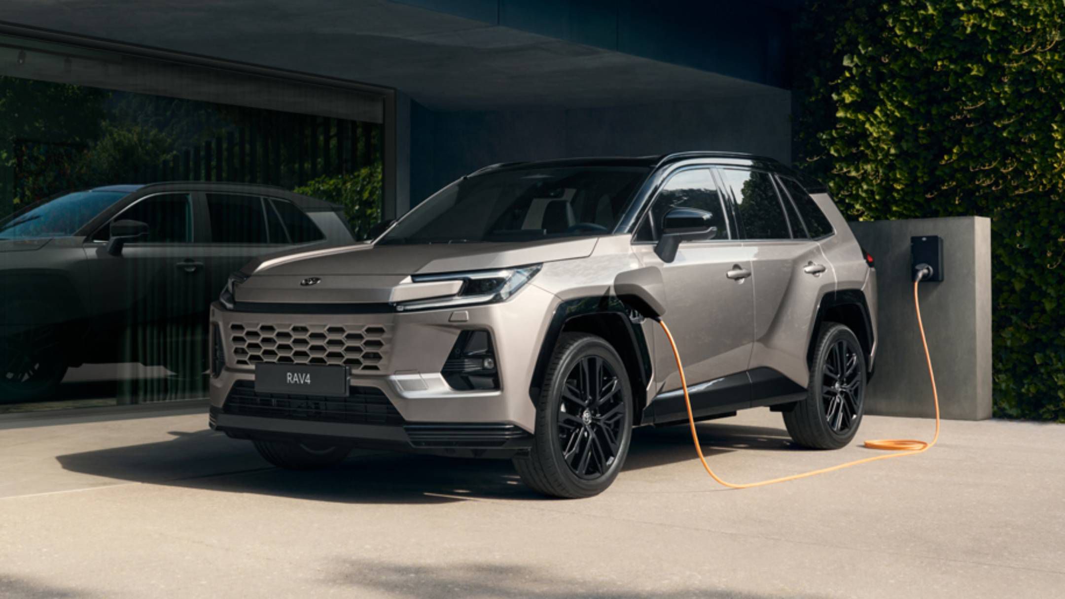 Silbernes Kompakt-SUV von Toyota steht überdacht in einer modernen Hauseinfahrt und lädt an einer Wallbox.