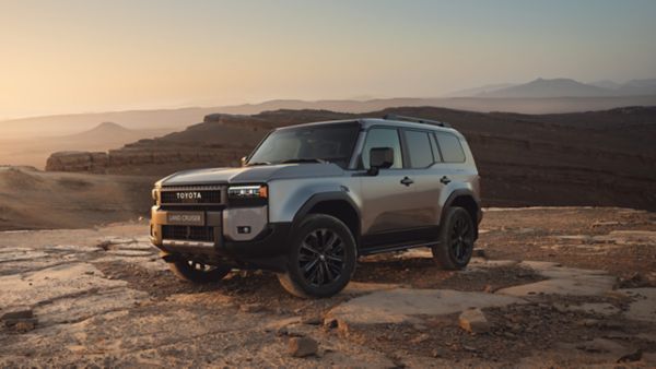 Ein Toyota Land Cruiser steht an einer Klippe in einer Wüstenlandschaft mit weiteren Berggipfeln in der Ferne