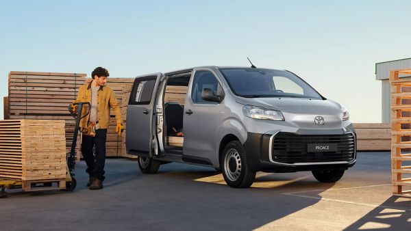 Ein Arbeiter in einer gelben Jacke steht in der Nähe eines silbernen Toyota Proace an einer Laderampe, die von Holzpaletten umgeben ist.