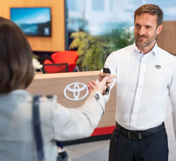 Toyota-Mitarbeiter in weißem Hemd übergibt einer Kundin im Showroom freundlich den Fahrzeugschlüssel.