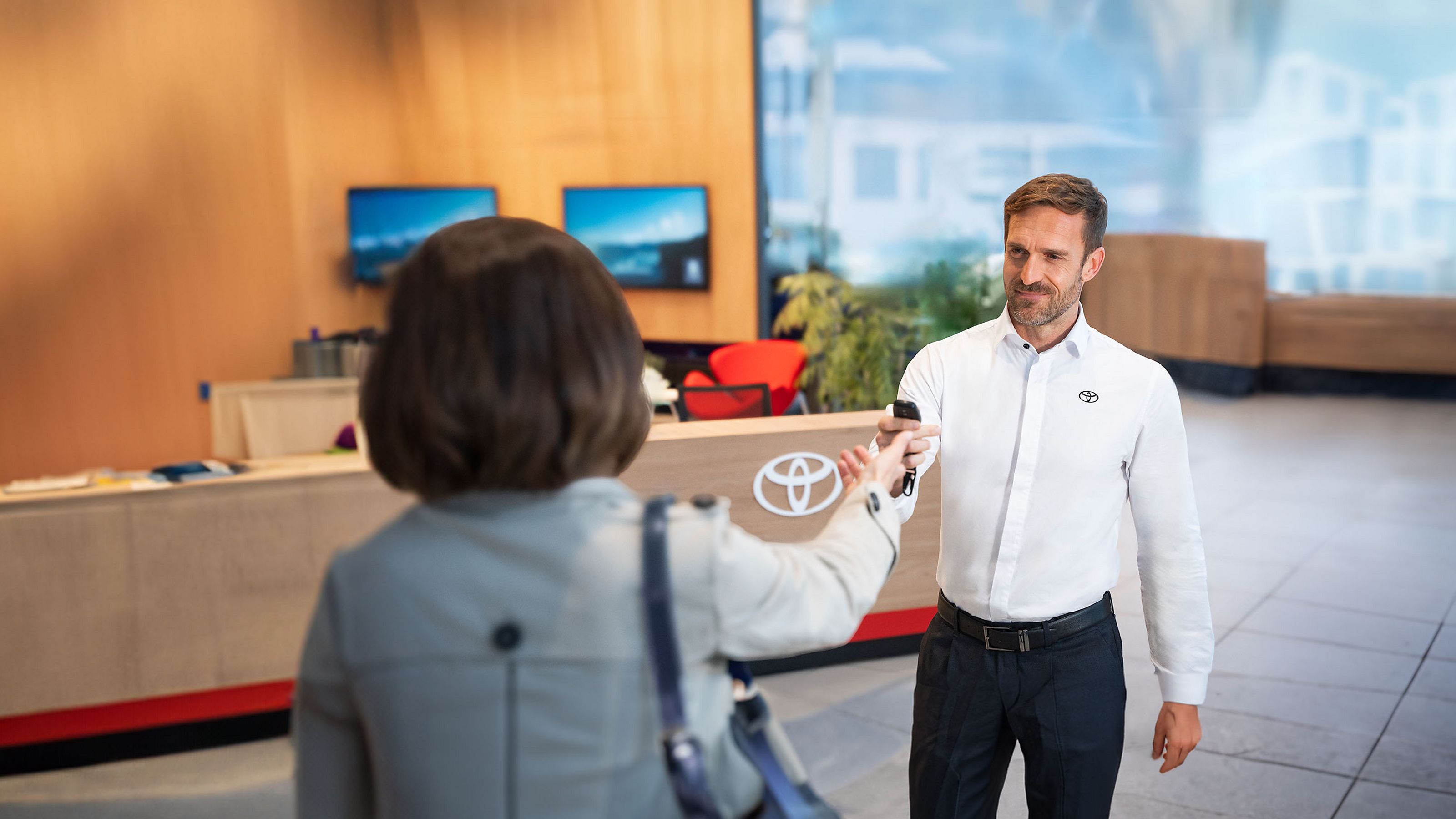 Toyota-Mitarbeiter in weißem Hemd übergibt einer Kundin im Showroom freundlich den Fahrzeugschlüssel.