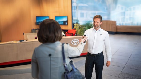 Toyota-Mitarbeiter in weißem Hemd übergibt einer Kundin im Showroom freundlich den Fahrzeugschlüssel.