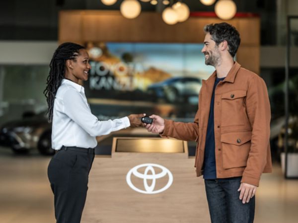 Händlerin übergibt einen Autoschlüssel an einen Kunden in einem Autohaus