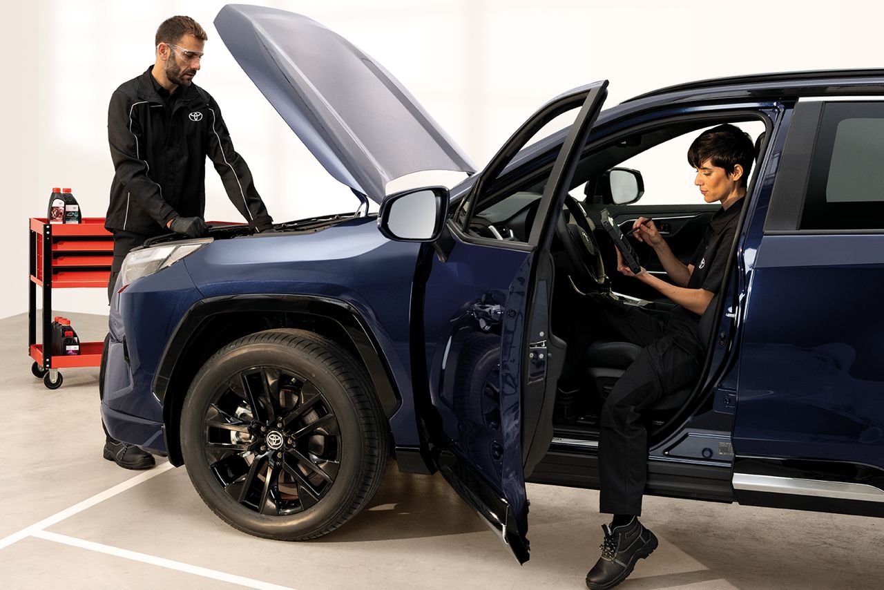 Zwei Personen arbeiten an einem roten Fahrzeug von Toyota, das in einer Werkstatt steht. Die Personen tragen einen Overall.