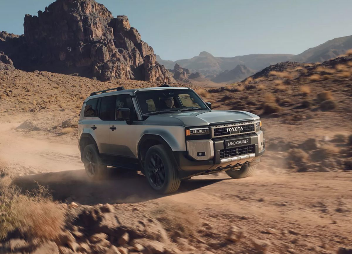 Silberner Toyota Land Cruiser fährt auf einer unbefestigten Wüstenstraße.