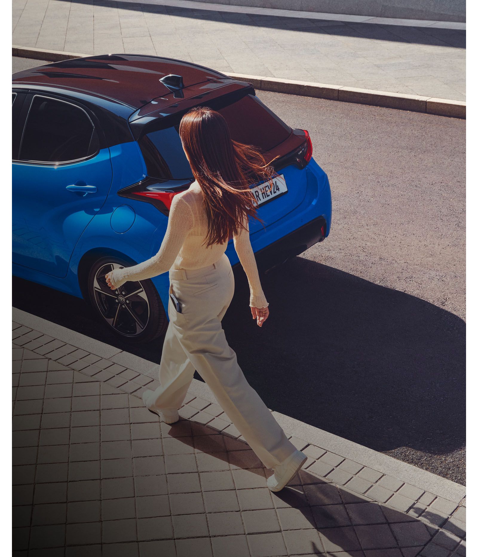 Une femme marche vers une Yaris stationnée, avec un effet visuel qui illustre la connectivité entre son téléphone et le déverrouillage de la voiture.