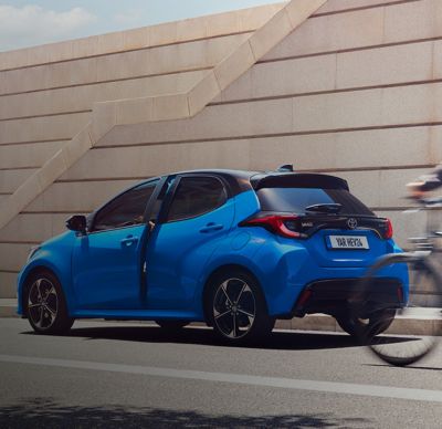 Rear 3/4 of the Toyota Yaris, driver's door opening and ciclist approaching the car