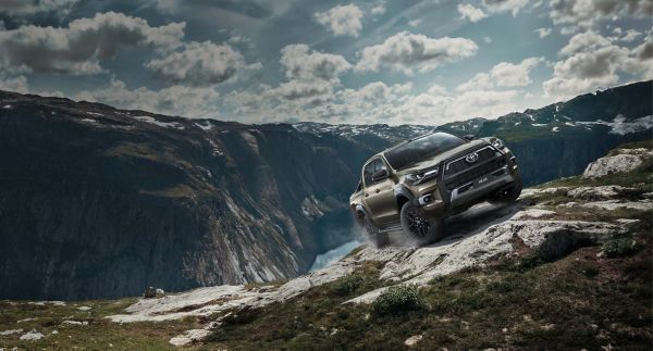 Ein Geländewagen, der durch felsiges Gelände fährt, mit einer atemberaubenden Berglandschaft und einem bewölkten Himmel im Hintergrund.