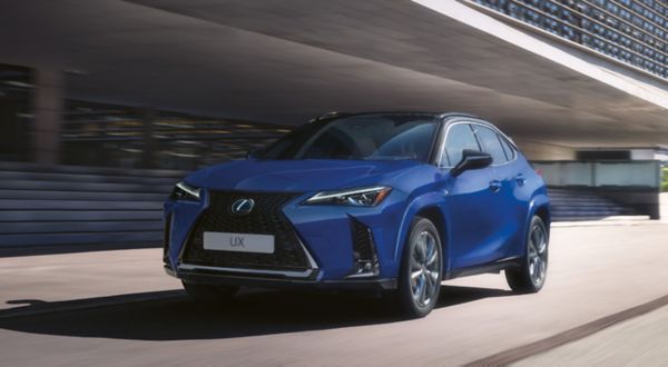 Ein blauer Lexus UX fährt an einem modernen Gebäude vorbei