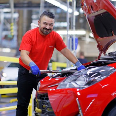 un homme souriant travaillant à l'usine tmmf qui tient une clé dynamométrique sur un moteur de toyota yaris